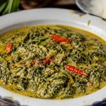 Semangkuk gulai daun singkong santan kental dengan cabai merah dan aroma rempah khas masakan Nusantara.