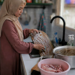 Ilustrasi seseorang membersihkan panci dan talenan bekas olahan daging kurban di dapur.