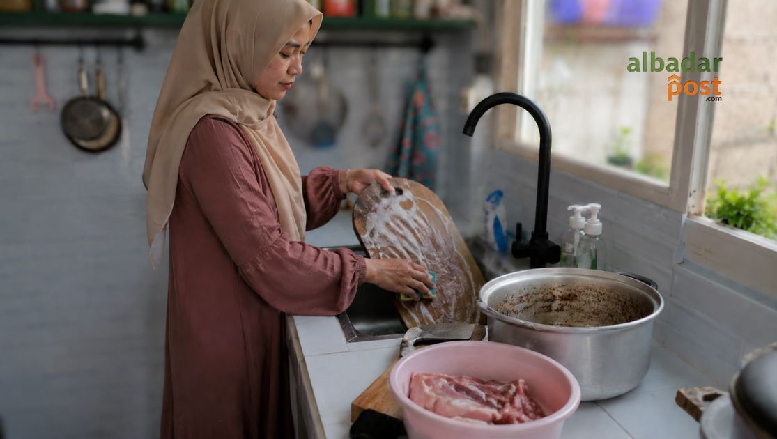 Ilustrasi seseorang membersihkan panci dan talenan bekas olahan daging kurban di dapur.